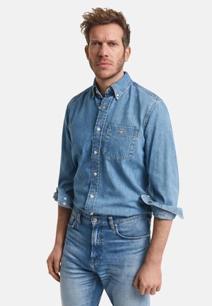 Denimskjorte i falmet blå med lange ærmer, knaplukket krave og en enkelt brystlomme. Båret med matchende lyseblå jeans.