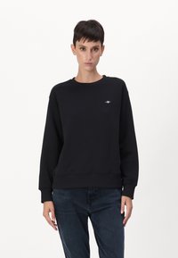 Svart hettegenser laget av bomullsblanding, med lange ermer, rund hals, ribbede mansjetter og en liten logo på brystet. Flat tekstur.