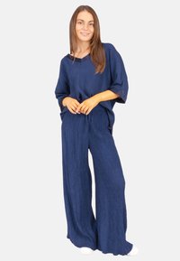 Haut bleu marine, ample, avec un col en V et des manches larges, associé à un pantalon large à taille haute et plis ; texture de tissu lisse.