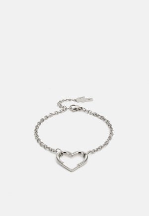 Sølv armbånd med kjededesign og et hjerteformet anheng. Hjertet er åpent, noe som fremhever den strømlinjeformede, moderne formen.