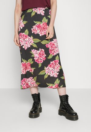 Saia maxi floral em preto com padrão de flores rosas e verdes, cintura elástica; usada com botas pretas de atacadores. Textura de tecido suave.
