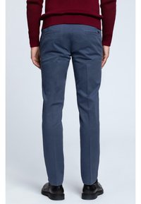Chino blu navy con una texture liscia, gambe affusolate, due tasche posteriori e design frontale piatto, indossati con scarpe nere.