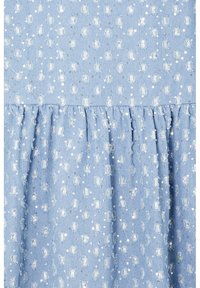 Tissu bleu clair avec couture froncée, décoré de points blancs texturés et de petits paillettes argentées brillantes disposées de manière éparse.