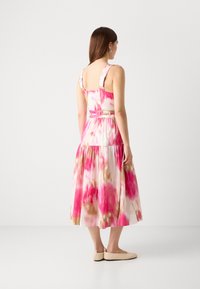 Robe midi en coton présentant un motif floral rose et crème, des bretelles larges, un corsage ajusté, et une jupe à étages avec une silhouette évasée.