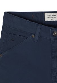Pantalones de hombre en azul marino con una textura de tela suave, que cuentan con un bolsillo frontal, cierre de botón y detalles metálicos en los bolsillos.