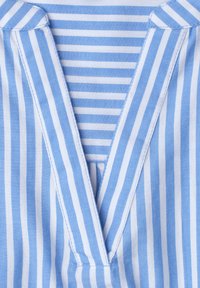 Cuello de camisa a rayas verticales en azul y blanco con apertura en forma de V, superpuesto sobre una tela a rayas horizontales en azul y blanco.