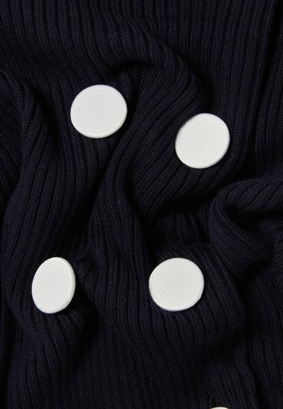 Tissu côtelé bleu marine avec cinq boutons ronds blancs. La texture est douce et serrée, mettant en avant une apparence épurée.