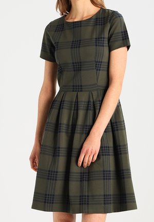 Frau trägt ein knielanges, kurzärmeliges Kleid mit dunkelgrünem und marineblauem Karomuster, tailliert und mit rundem Ausschnitt.