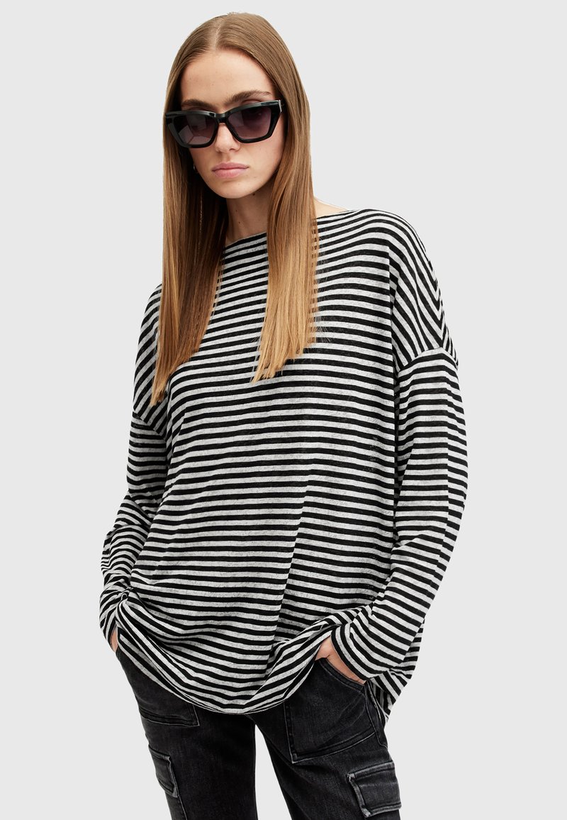 Camicia oversize a righe bianche e nere con una vestibilità comoda e maniche lunghe, abbinata a pantaloni cargo scuri e occhiali da sole neri angolari.