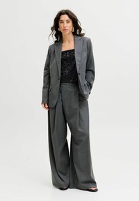 Pelēks rūtainais pielāgotais žakets, apvienots ar platām pelēkām biksēm, virs melna mirdzoša topa. Gluda auduma, strukturēts dizains un smalka spīduma.