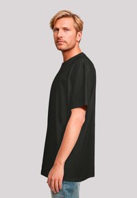 Zwarte katoenen t-shirt met een relaxte pasvorm, korte mouwen en een ronde hals, getoond op een model van de zijkant tegen een neutrale achtergrond.