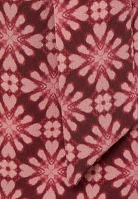 Röd tyg med ett blommigt och hjärtformigt mönster i rosa nyanser, med en texturerad yta och mjukt fall. Inkluderar ett vikt kantdetalj.