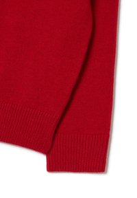 Close-up of the sleeve and cuff of a red knitted sweater with ribbed edges on a white background.