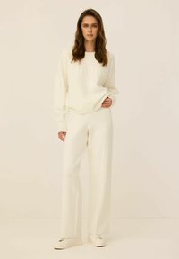 Biała bluza z wyszytym napisem "ATHLETICS", w połączeniu z dopasowanymi, szerokimi białymi spodniami i białymi sneakersami. Gładka faktura, minimalistyczny design.