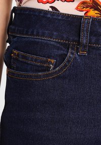 Jeans de mezclilla azul oscuro con un corte clásico, con costuras naranjas, un pequeño bolsillo delantero y un diseño de cintura alta.