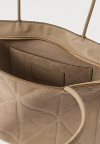 Beige velúrbőr táska geometrikus mintákkal, nyitott tetejű cipzárral, bőrkarral és belső zsebbel, amin Calvin Klein címke található.