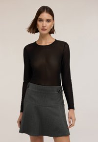 Schwarzes, transparentes Langarmoberteil kombiniert mit einem dunkelgrauen A-Linien-Rock mit Knopfdetails, der ein texturiertes und mehrschichtiges Erscheinungsbild schafft.