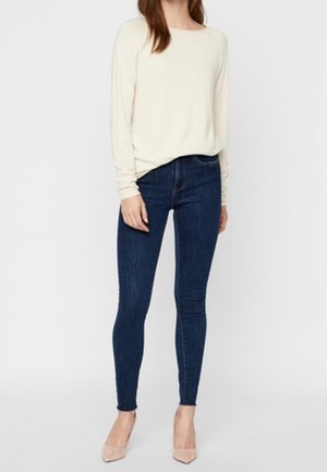 Light cream long-sleeve top paired with dark blue skinny jeans and nude high heels. The top has a relaxed fit and a round neckline.