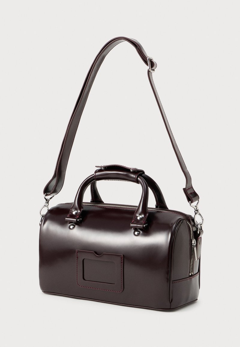 Piccola borsa bordeaux realizzata in ecopelle lucida, con doppi manici, una tracolla removibile e una tasca frontale con patta.