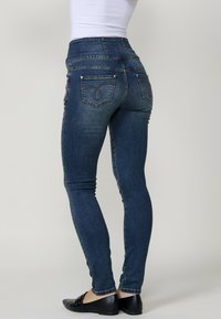 Jeans ajustados de mezclilla azul oscuro con cintura media, que cuentan con bolsillos traseros y sutiles detalles bordados. Textura suave y forma ajustada.