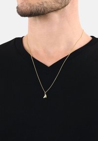 Uomo che indossa una maglietta nera a V e una collana d'oro con un ciondolo a forma di lettera A appesa al collo.