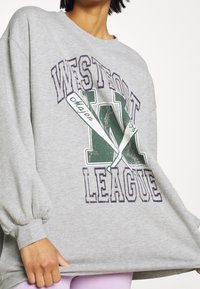 Šedá mikina s velkým potiskem "WEST" a "LEAGUE" v purpurové a zelené barvě, s volným střihem a nafouklými rukávy.