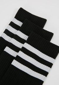 Schwarze Socken mit drei horizontalen weißen Streifen. Rippstruktur. Standard Crew-Länge. Weiches Material, geeignet für Freizeitkleidung oder Sport.