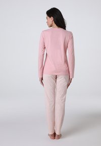 Top a maniche lunghe rosa chiaro abbinato a pantaloni rosa chiaro a fantasia con un discreto motivo a foglia. Il tessuto appare liscio e ha una vestibilità rilassata.