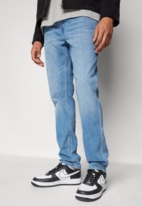 Jeans de mezclilla azul claro con corte recto, con costuras visibles y combinados con zapatillas Nike en blanco y negro.