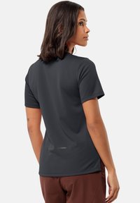 T-shirt noir à manches courtes avec un col rond, texture lisse et un accent discret à l'arrière. Porté avec un pantalon marron.
