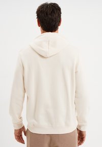 Kremowy hoodie z centralnym szwem na plecach, prążkowanymi mankietami i kapturem ze sznurkiem. Wykonany z miękkiej, teksturowanej tkaniny.