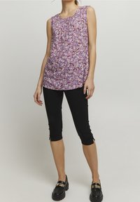 Ærmeløs lilla top med blomsterprint, sammensnøring ved halsen, parret med sorte capri leggings og sorte loafers med guld accenter.