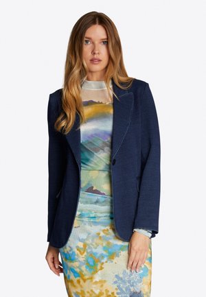 Navy blue blazer with notch lapels, single button closure, and two front pockets, worn over a multicolored patterned dress.