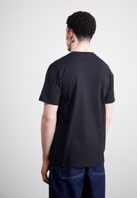 Černé bavlněné tričko s krátkým rukávem a kulatým výstřihem, z pohledu zezadu. Hladká textura s jednoduchým designem.