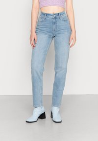 Jeans de cintura alta de tom azul claro com ajuste reto e lavagem desbotada, combinados com botas de tornozelo azul claro e uma blusa cropped canelada.