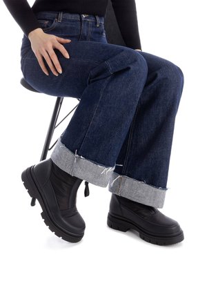 Stivali neri con suole spesse abbinati a jeans larghi di denim blu scuro, caratterizzati da un risvolto grigio a contrasto con bordi sfilacciati.