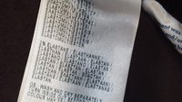 Ruhacímke, amely a szövet összetételét mutatja, főként poliészter és elasztán, részben látható ápolási utasításokkal az oldalán.