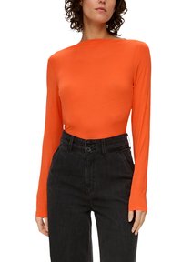 Oranges Langarmoberteil aus weichem Stoff mit einem Boot-Ausschnitt. Kombiniert mit hochtaillierten schwarzen Jeans aus Denim mit Knöpfen.