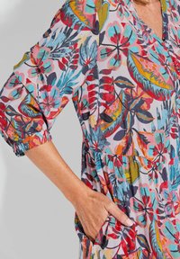 Bloemenprint jurk met levendige kleuren zoals rood, teal en geel. Lichtgewicht stof, met een v-hals ontwerp, gathered taille en zijzakken.