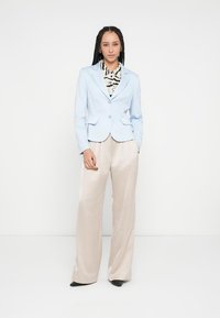 Blazer ajustado azul claro con dos botones, combinado con pantalones anchos beige. Debajo, una camisa estampada en blanco y negro.