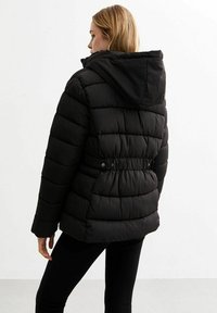 Veste doudoune noire avec capuche, dotée de coutures horizontales, d'une taille cintrée avec des boutons et d'un tissu texturé et isolant.