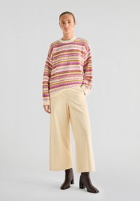 Pull en tricot avec des rayures roses, jaunes et crème, associé à un pantalon large en velours côtelé beige et des bottes à talons marron.