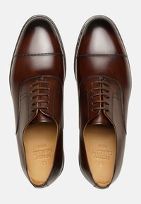Braune Lederanzugschuhe mit glatter Oberfläche, Kappe und Schnürung mit sechs Ösen. Helle, beige Innensohle mit geprägt Markenlogo.