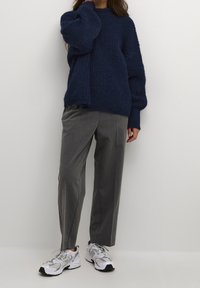 Niebieski sweter o teksturowanej powierzchni w oversize'owym kroju, szare spodnie o dopasowanym kroju oraz szaro-białe sneakersy sportowe. Prosty, nowoczesny design z luźnym krojem.