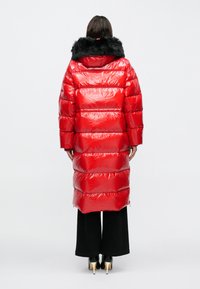 Piros felfújt kabát fényes felülettel, fekete szőrmével szegélyezett kapucnival, hosszú ujjakkal és térdig érő fazonnal.