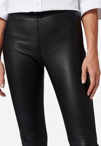 Zwarte nepleer leggings met een gladde textuur, hoge taille en slim fit, voorzien van gestikte naden en een glanzende afwerking.