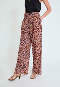 Pantalones de pierna ancha con estampado de leopardo en tonos marrones, naranjas y negros, con cintura alta y bolsillos laterales. Tejido suave y liso.