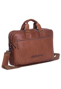 Valigetta di pelle marrone con due manici superiori, tracolla regolabile, tasca frontale con zip e logo del marchio impresso. Texture liscia, design rettangolare.