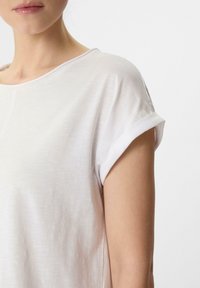 Biała bluzka krótki rękaw z podwiniętymi mankietami, wykonana z miękkiego, lekkiego materiału i z luźnym dekoltem w serek. Gładka tekstura i prosty design.