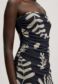 Trägerloses Kleid aus dunkelblauem Stoff mit cremefarbenen Blättermustern. Strukturiertes Raffung an der Seite betont die Form und Silhouette.